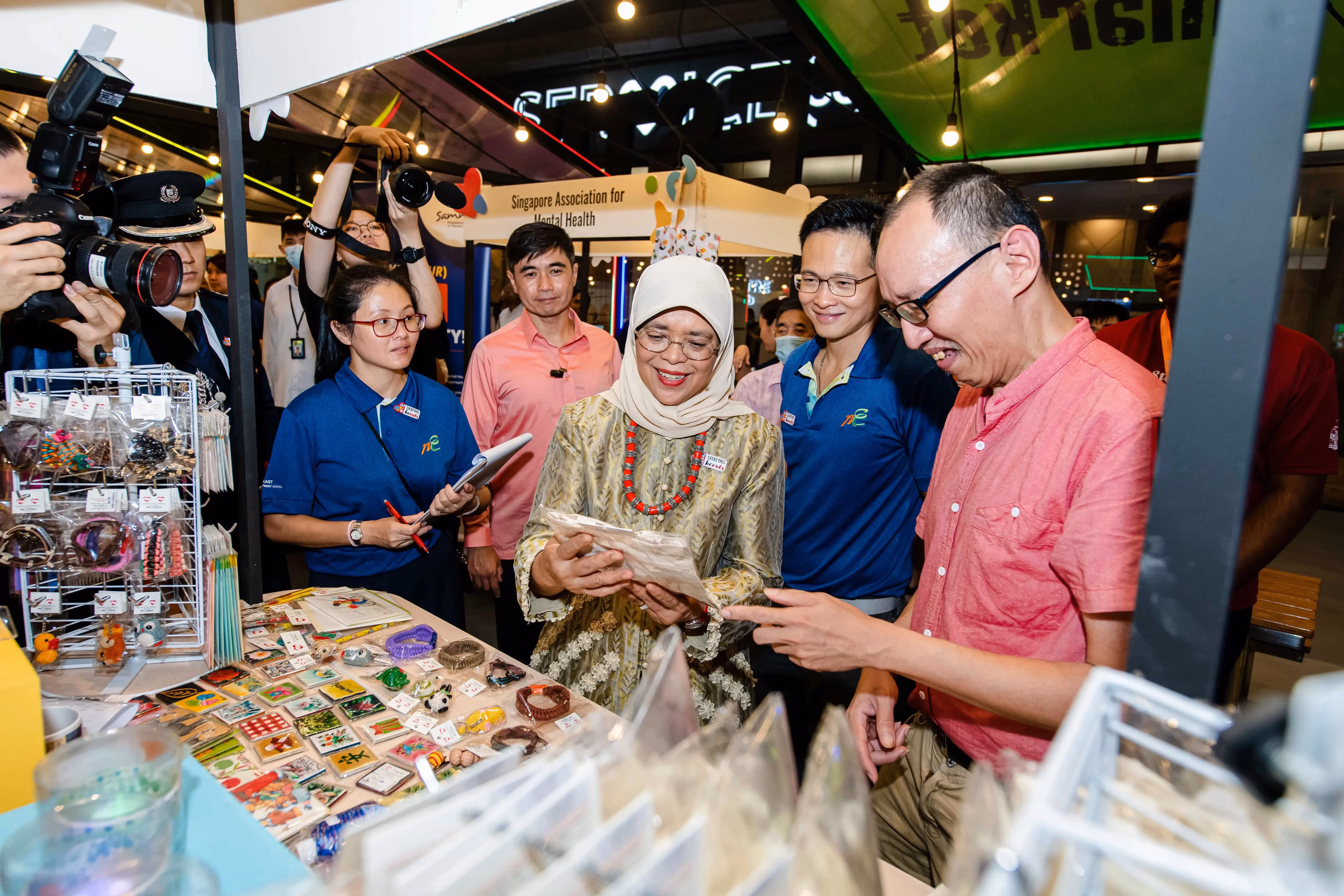A group of people gather around a table displaying various colourful items at Shaping Hearts event booth.